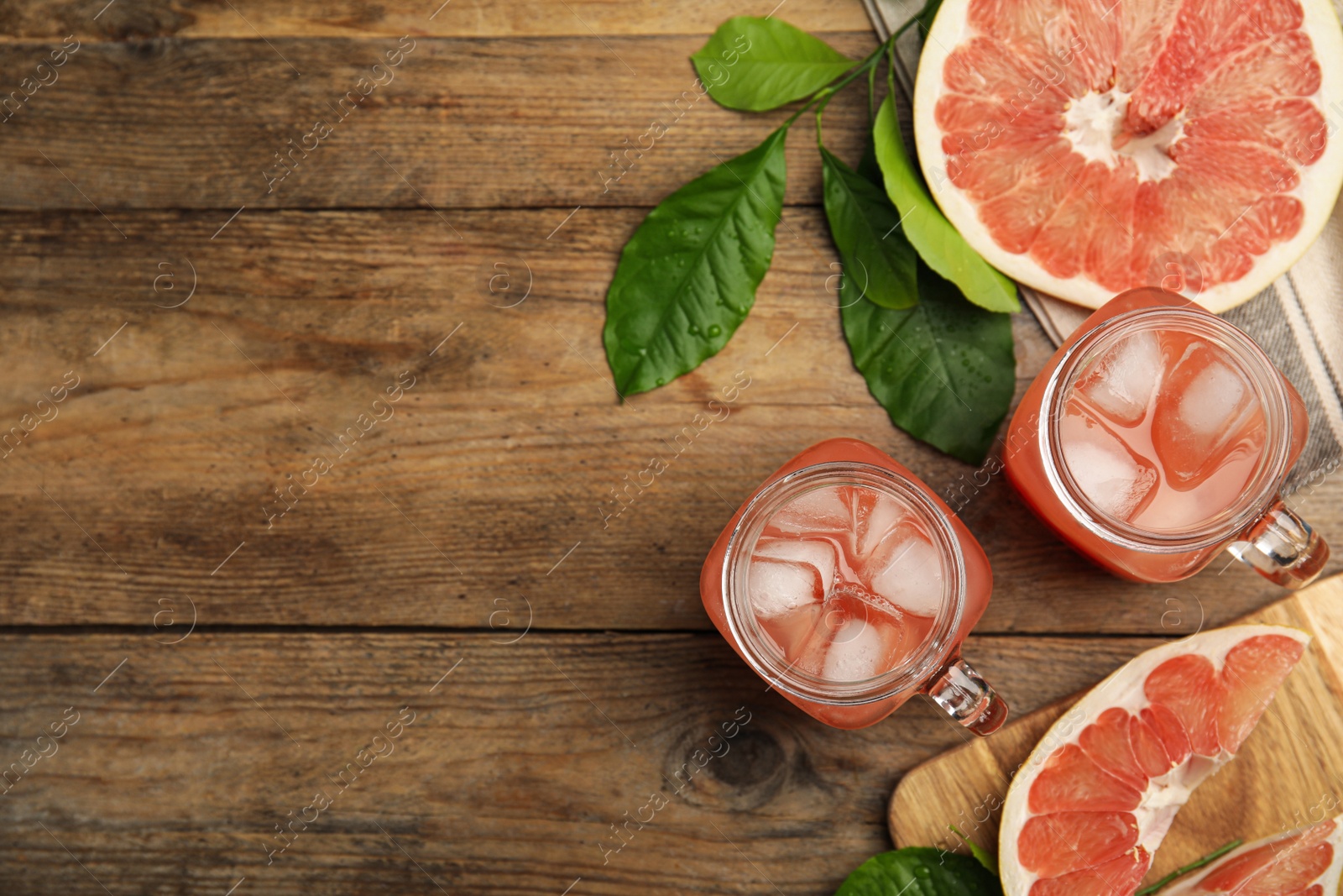 Photo of Glass jars of cold pomelo juice and fruit on wooden table, flat lay. Space for text