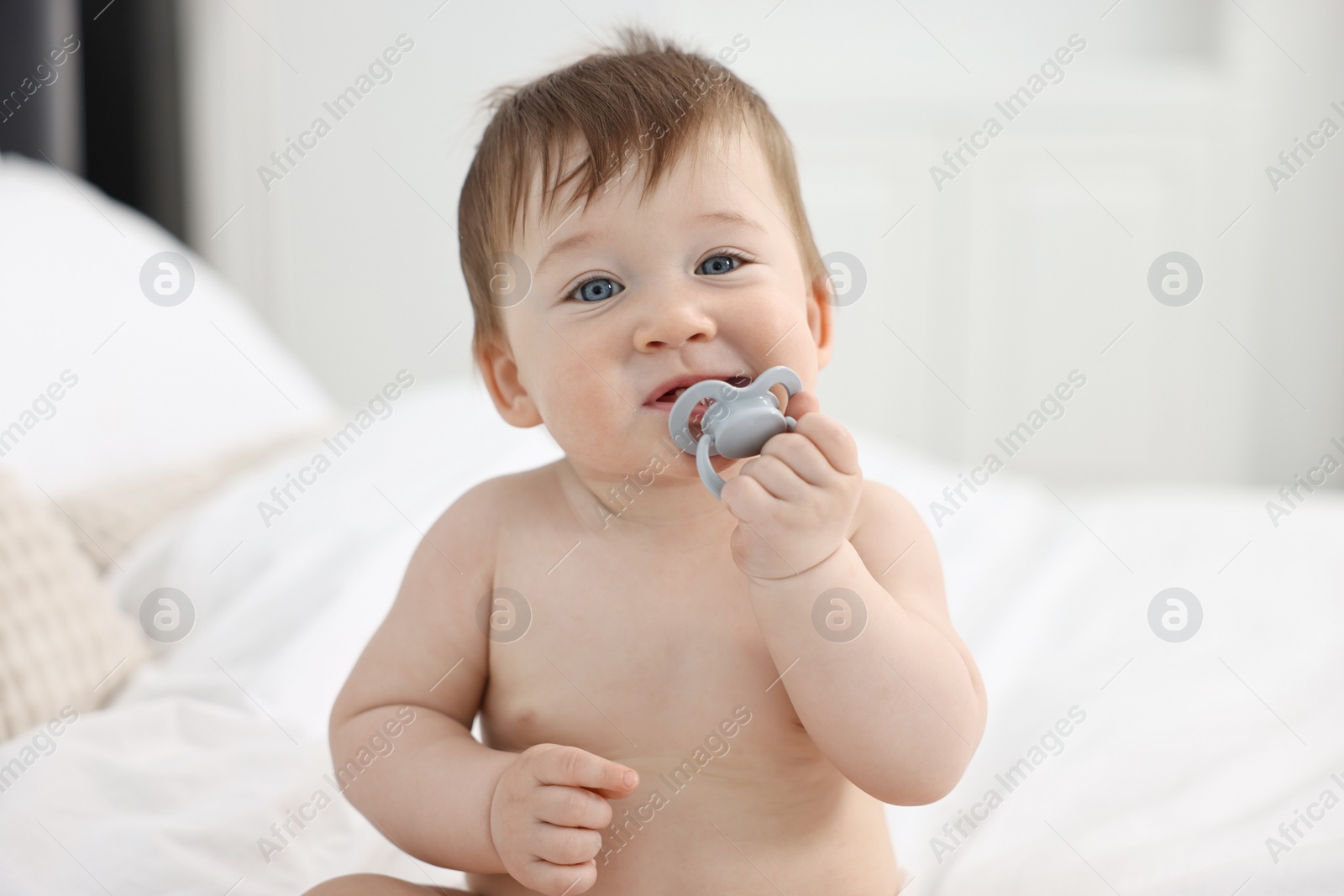Photo of Cute baby boy with pacifier on bed at home