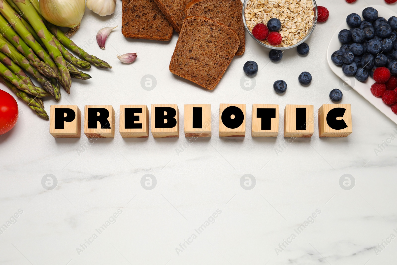 Photo of Flat lay composition of wooden cubes with word Prebiotic and food on white marble table. Space for text