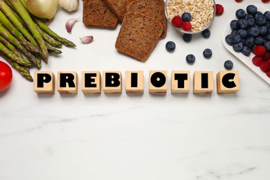 Flat lay composition of wooden cubes with word Prebiotic and food on white marble table. Space for text