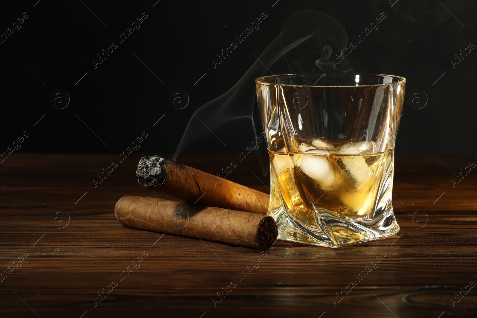 Photo of Glass of whiskey with ice cubes and cigars on wooden table