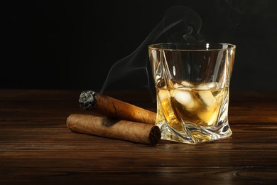 Glass of whiskey with ice cubes and cigars on wooden table