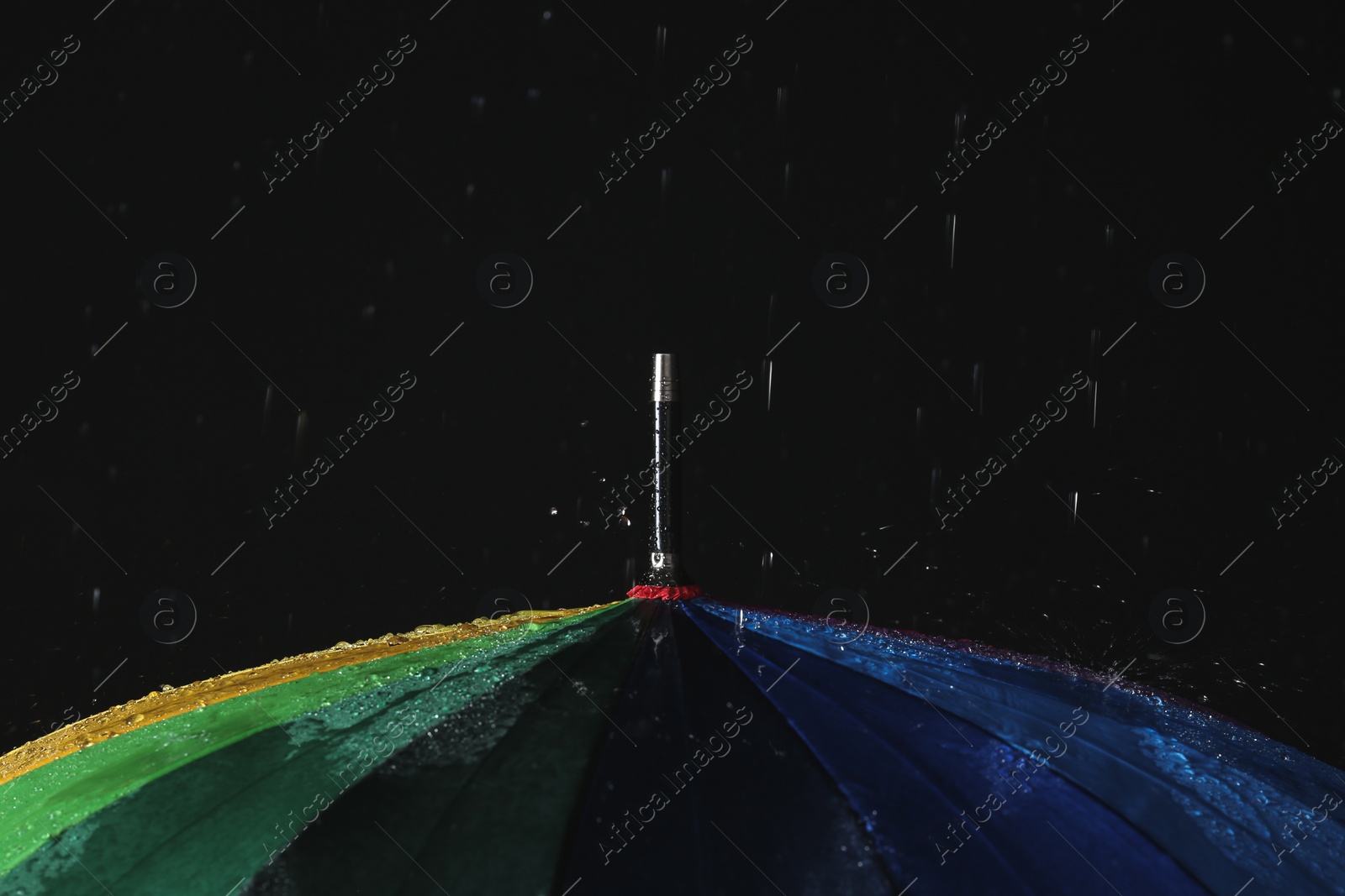 Photo of Opened color umbrella under rain against black background, closeup