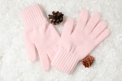 Photo of Stylish pink woolen gloves and fir cones on artificial snow, flat lay