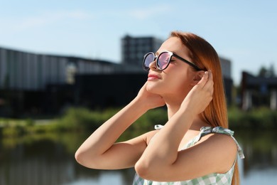 Beautiful woman in sunglasses near river, space for text