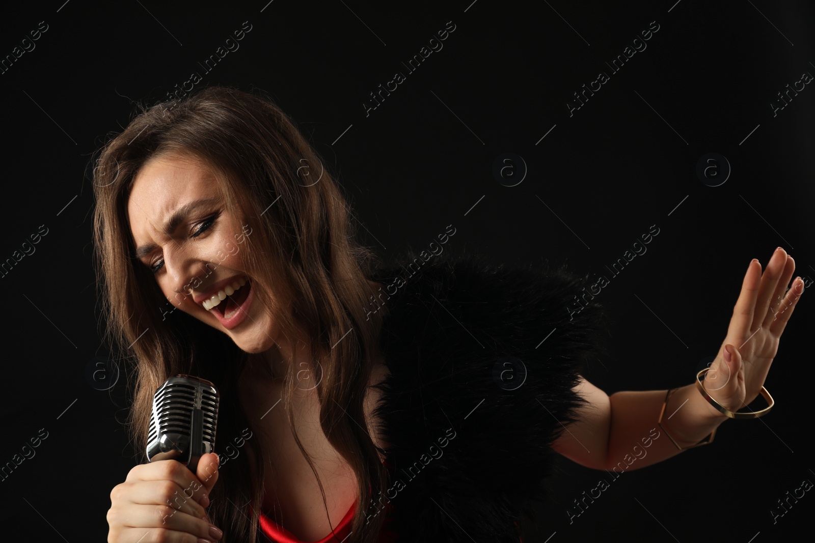 Photo of Beautiful young woman with microphone singing on black background