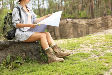 Photo of Young woman with map sitting on rock in forest. Camping season