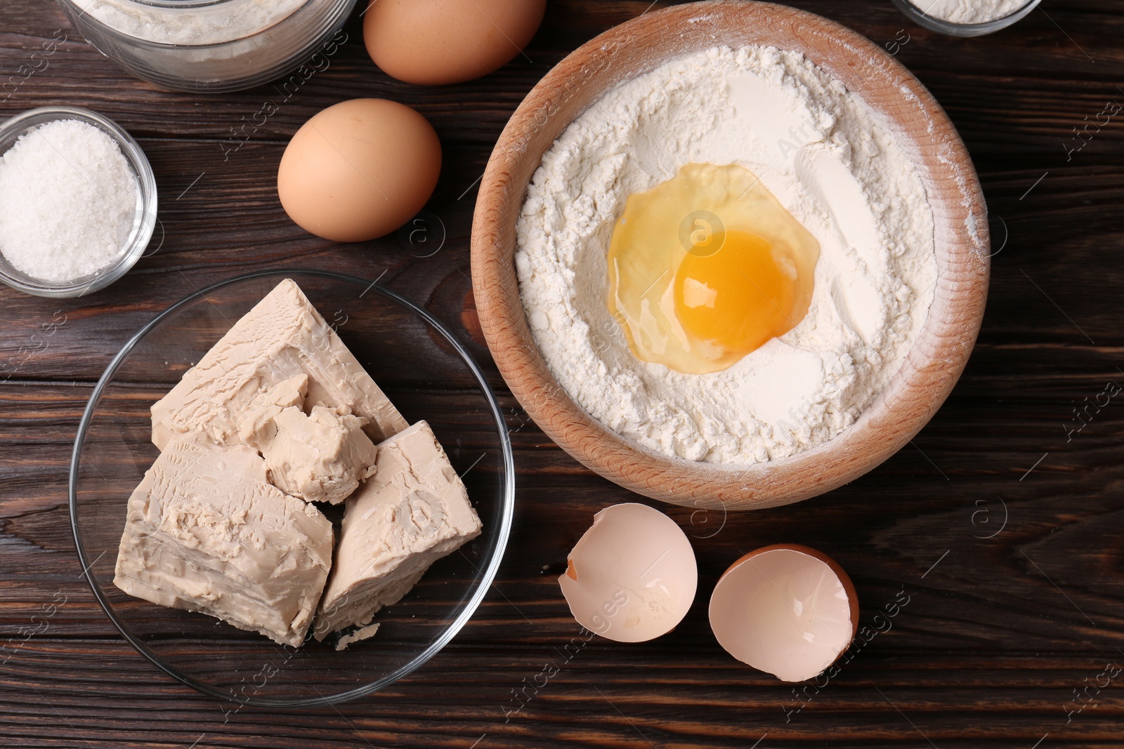 Photo of Compressed yeast, flour, salt and eggs on wooden table, flat lay