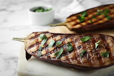 Delicious grilled eggplant halves with parsley on white marble table, closeup