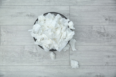 Used paper tissues in trash can on wooden floor, flat lay