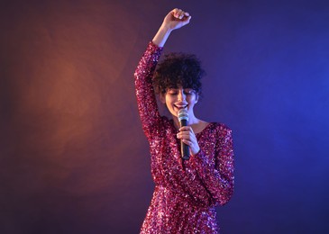 Beautiful young woman with microphone singing on color background in neon lights