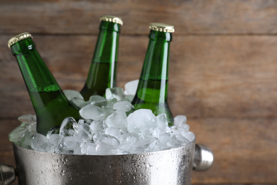 Photo of Metal bucket with beer and ice cubes on wooden background, closeup