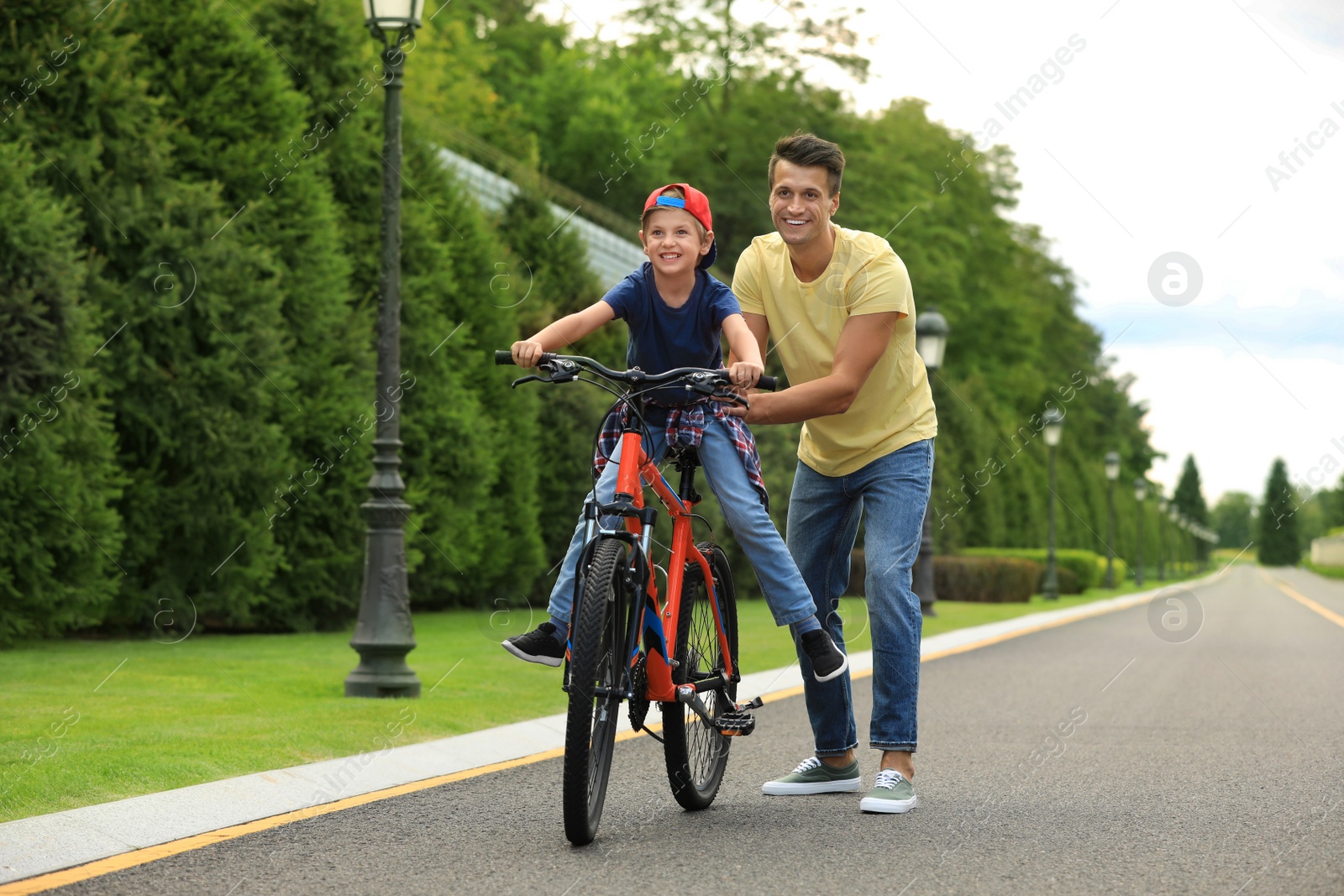 Image of Dad teaching son to ride bicycle outdoors