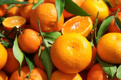 Photo of Many ripe tangerines with leaves as background, closeup