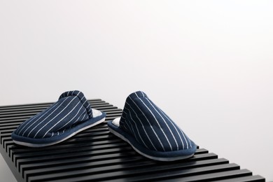 Photo of Pair of stylish slippers on bench against light grey background