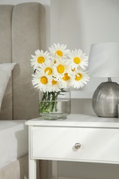 Photo of Bouquet of beautiful daisy flowers and lamp on nightstand in bedroom