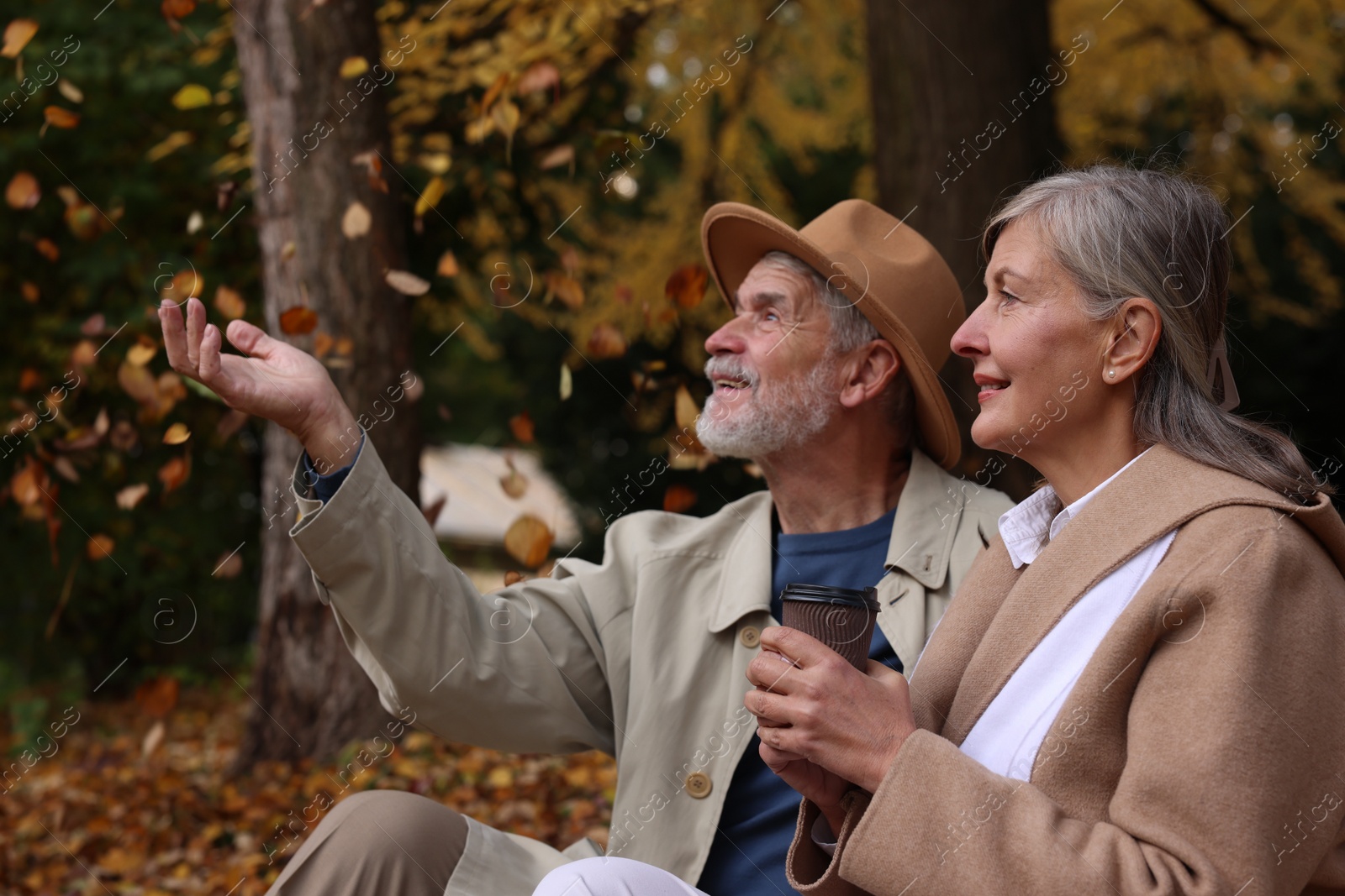 Photo of Affectionate senior couple with cup of coffee in autumn park