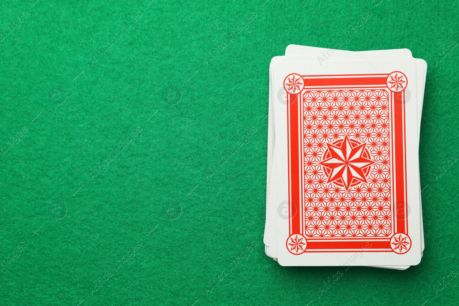 Photo of Deck of playing cards on green table, top view. Space for text