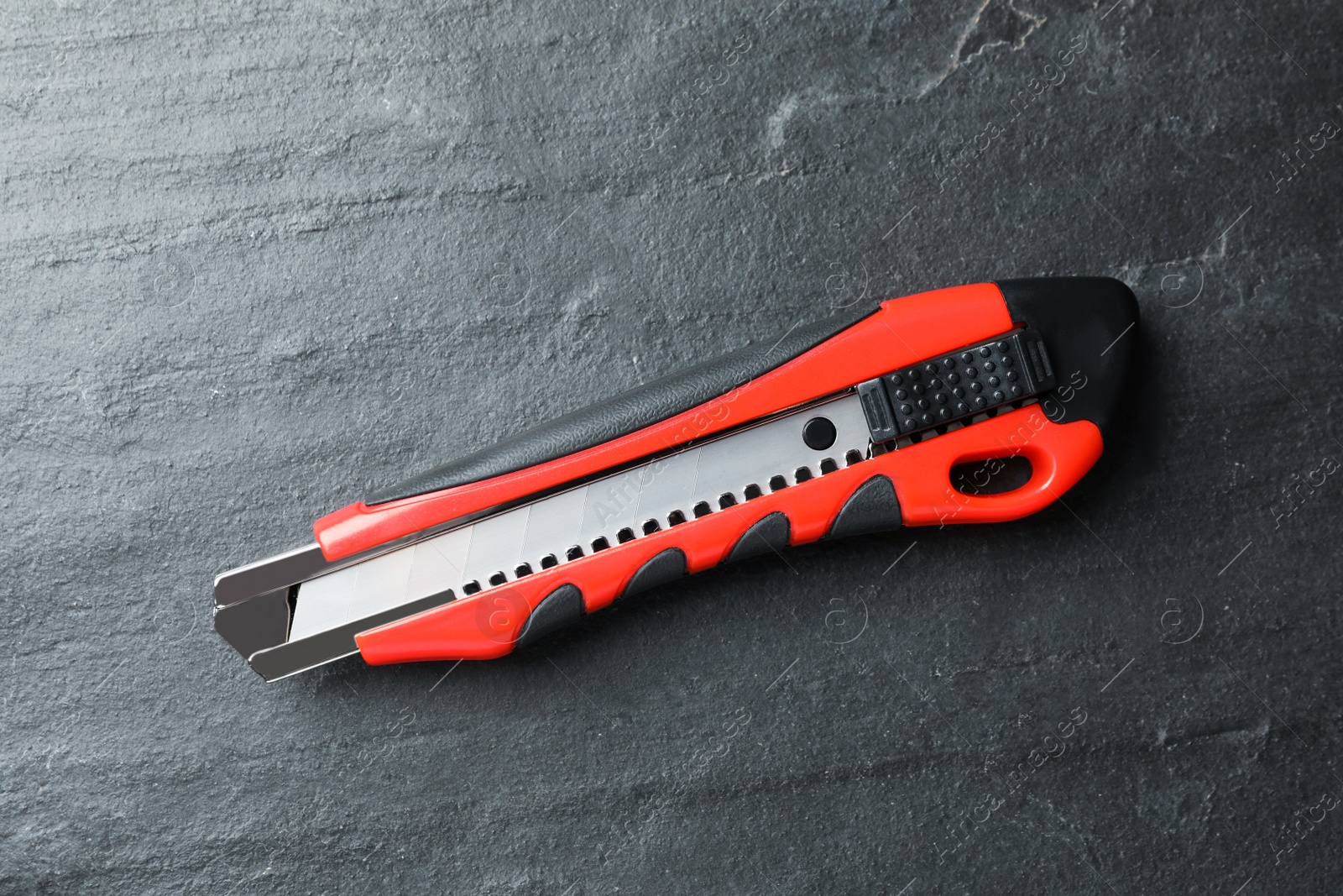 Photo of Utility knife on black table, top view. Construction tool