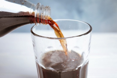 Pouring refreshing soda drink into glass on table, closeup