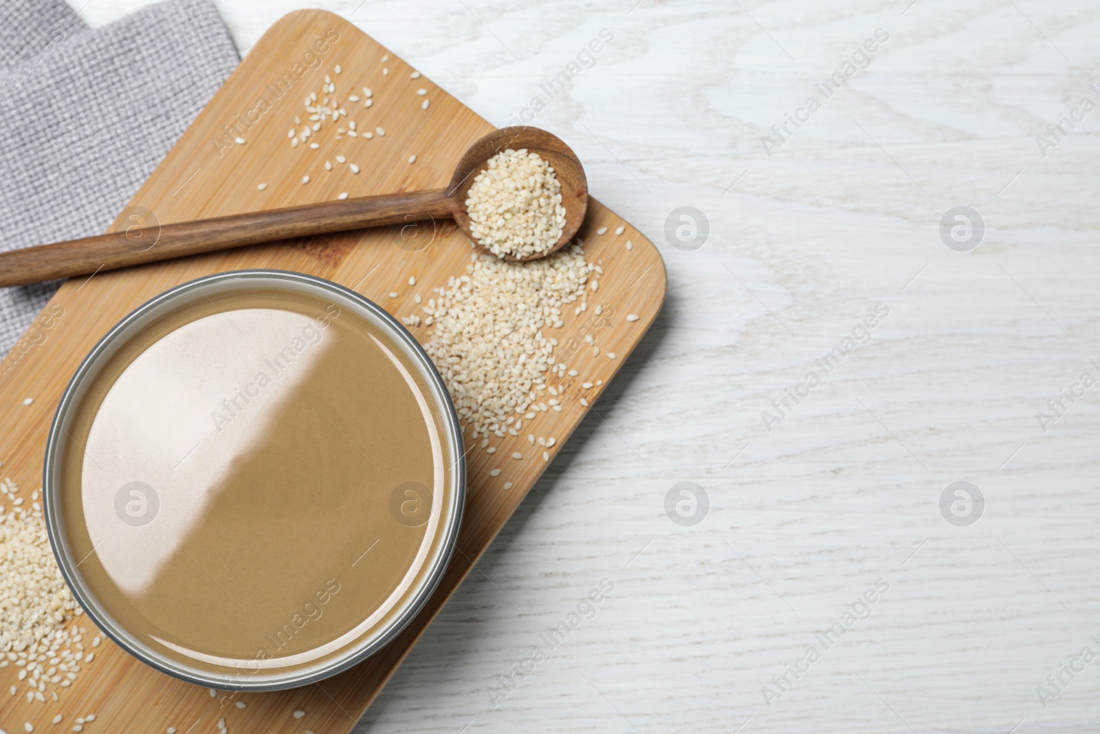 Photo of Tasty sesame paste, seeds and spoon on white wooden table, top view. Space for text