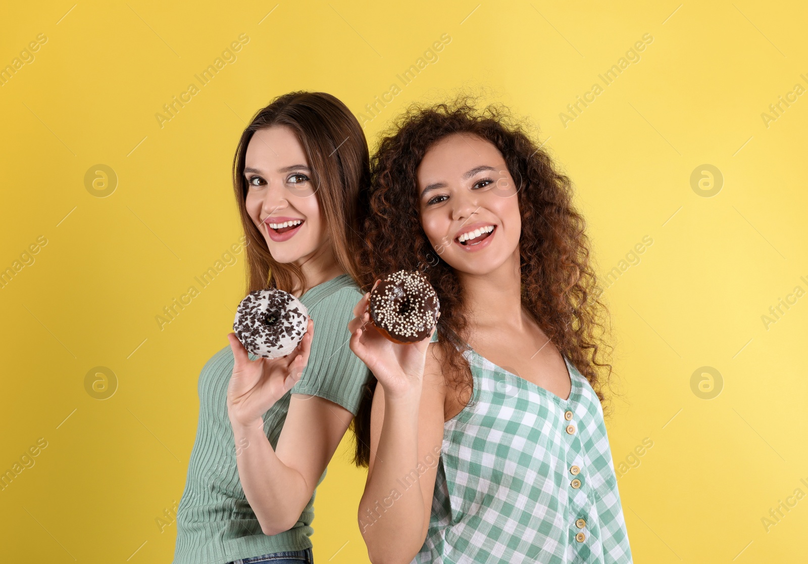 Photo of Beautiful young women with donuts on yellow background