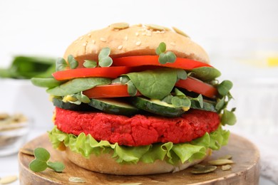 Photo of Tasty vegan burger with vegetables, patty and microgreens on wooden board, closeup