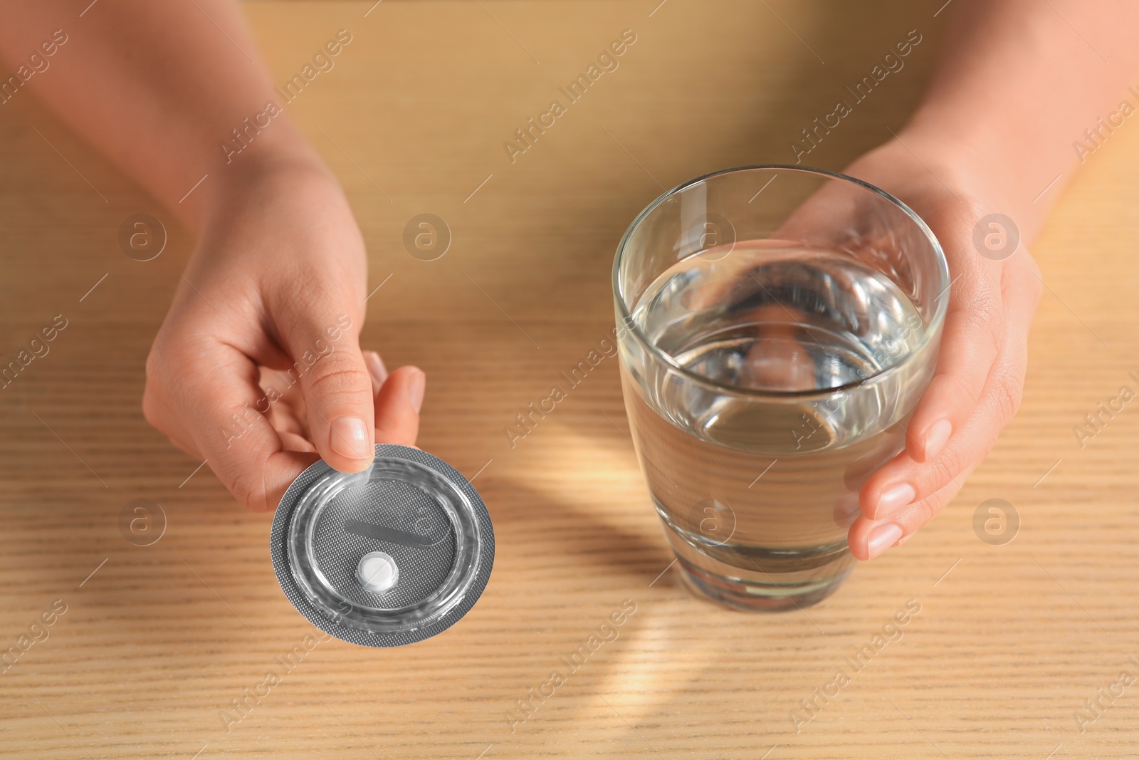 Photo of Woman taking emergency contraception pill at wooden table indoors, closeup