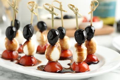 Photo of Tasty canapes with black olives, mozzarella and cherry tomatoes on white marble table, closeup
