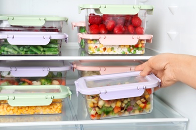 Photo of Woman taking box with vegetable mix from refrigerator, closeup