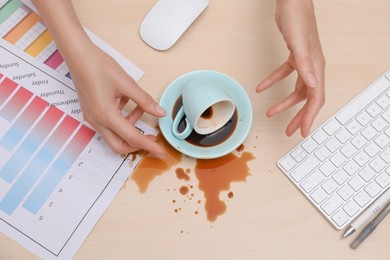 Photo of Closeup of woman spilled coffee on wooden office desk, top view