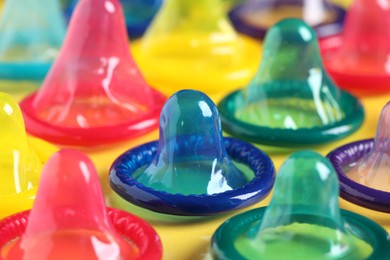 Colorful condoms on yellow background, closeup view