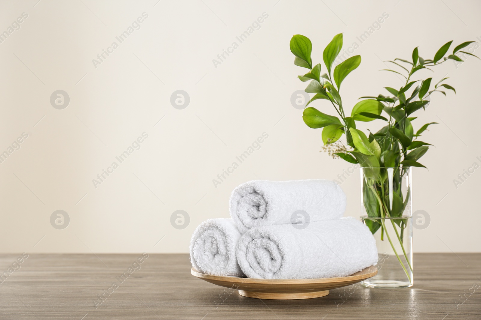 Photo of Fresh rolled towels and green branches on grey wooden table