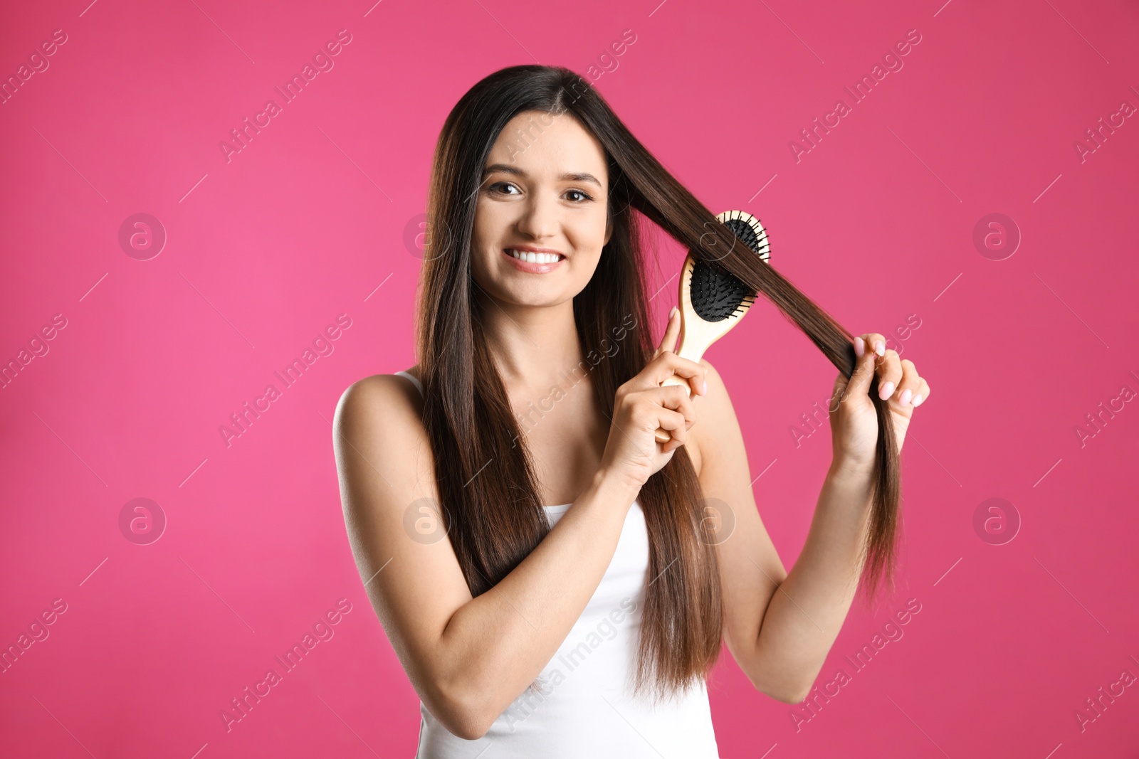 Photo of Beautiful smiling young woman with hair brush on color background