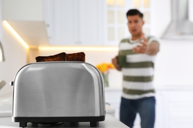 Photo of Emotional man preparing breakfast in kitchen, focus on toaster with slices of burnt bread
