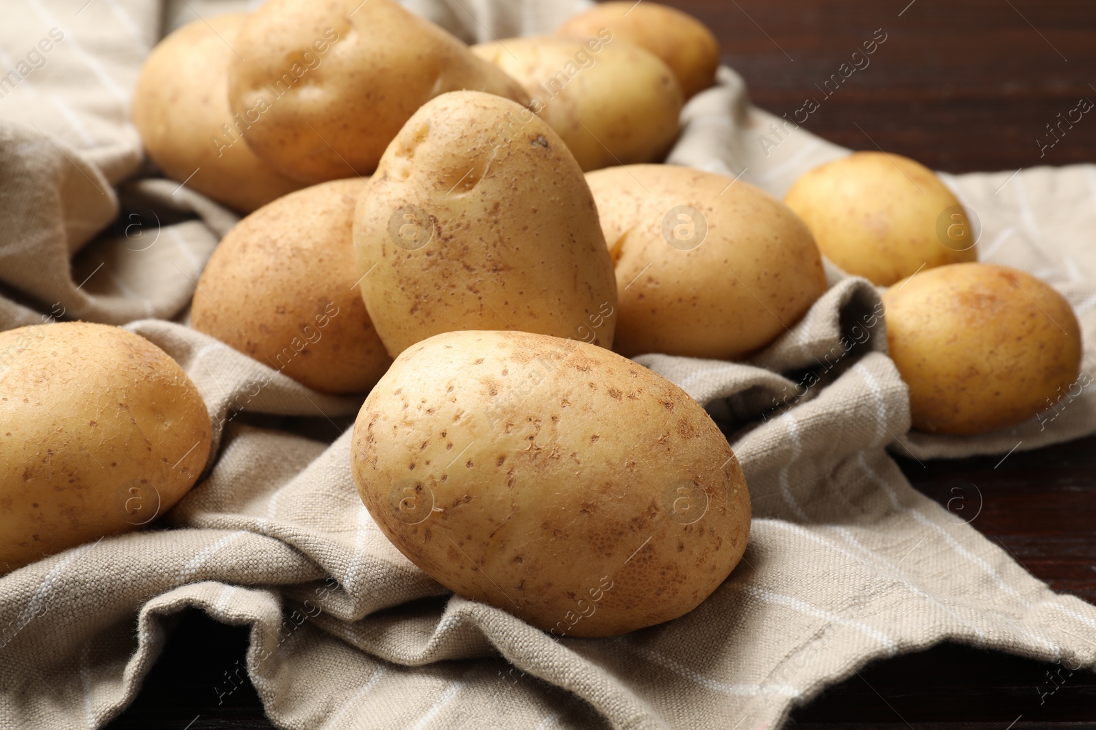 Photo of Raw fresh potatoes and napkin on wooden table, closeup