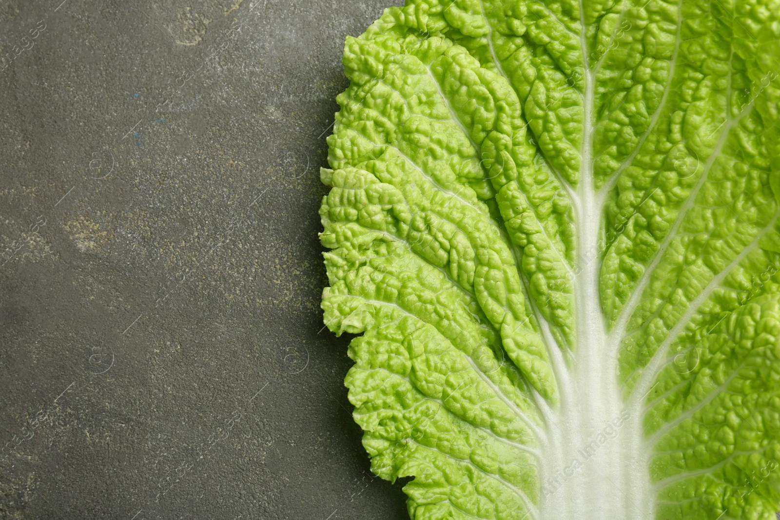 Photo of Fresh Chinese cabbage leaf on gray textured table, top view. Space for text