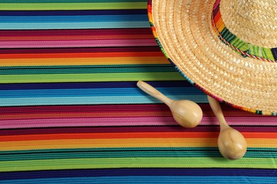Mexican sombrero hat and maracas on color table, top view. Space for text