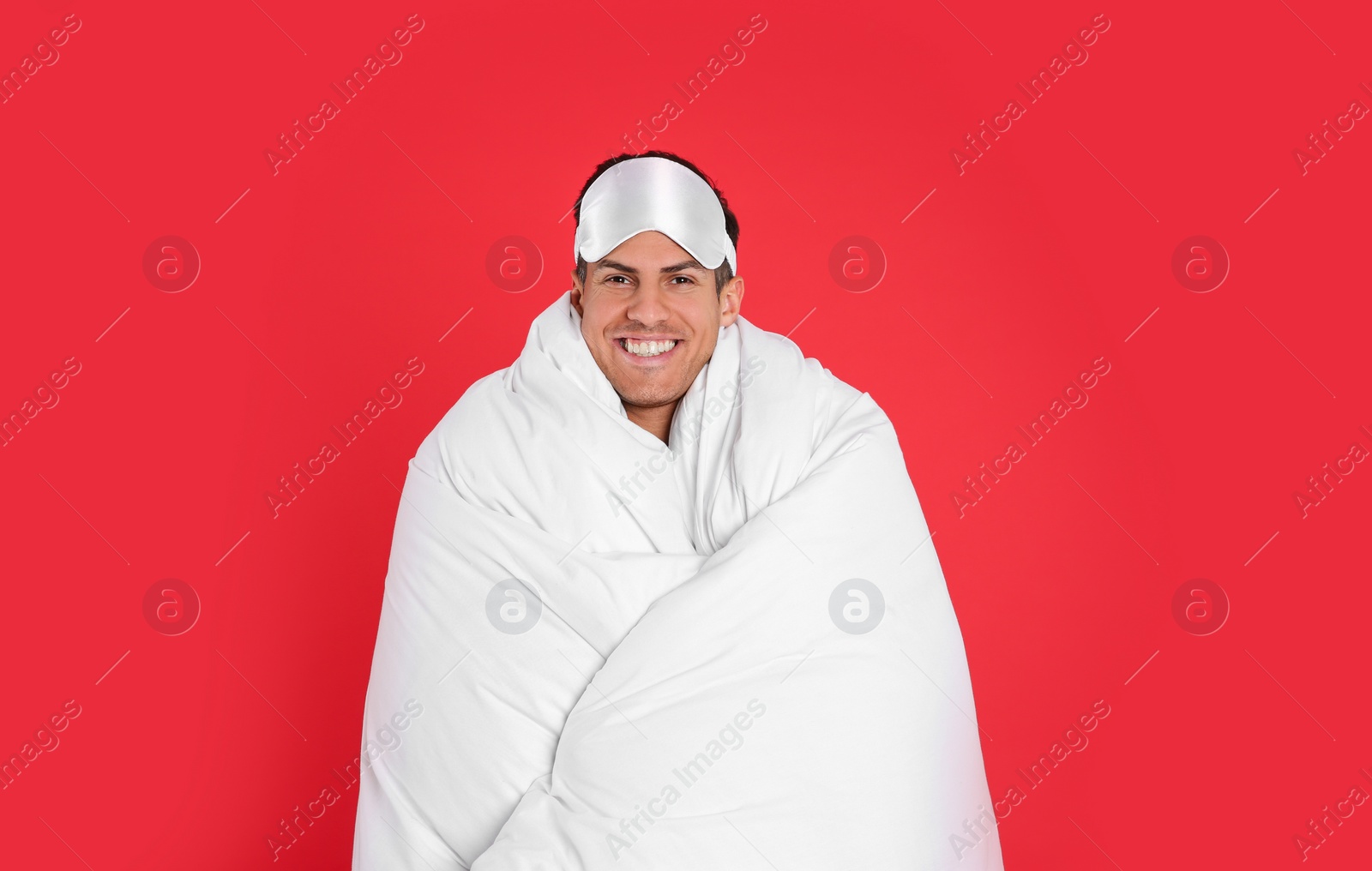 Photo of Man in sleeping mask wrapped with blanket on red background