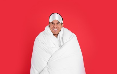 Photo of Man in sleeping mask wrapped with blanket on red background