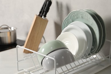 Drainer with different clean dishware on white table indoors