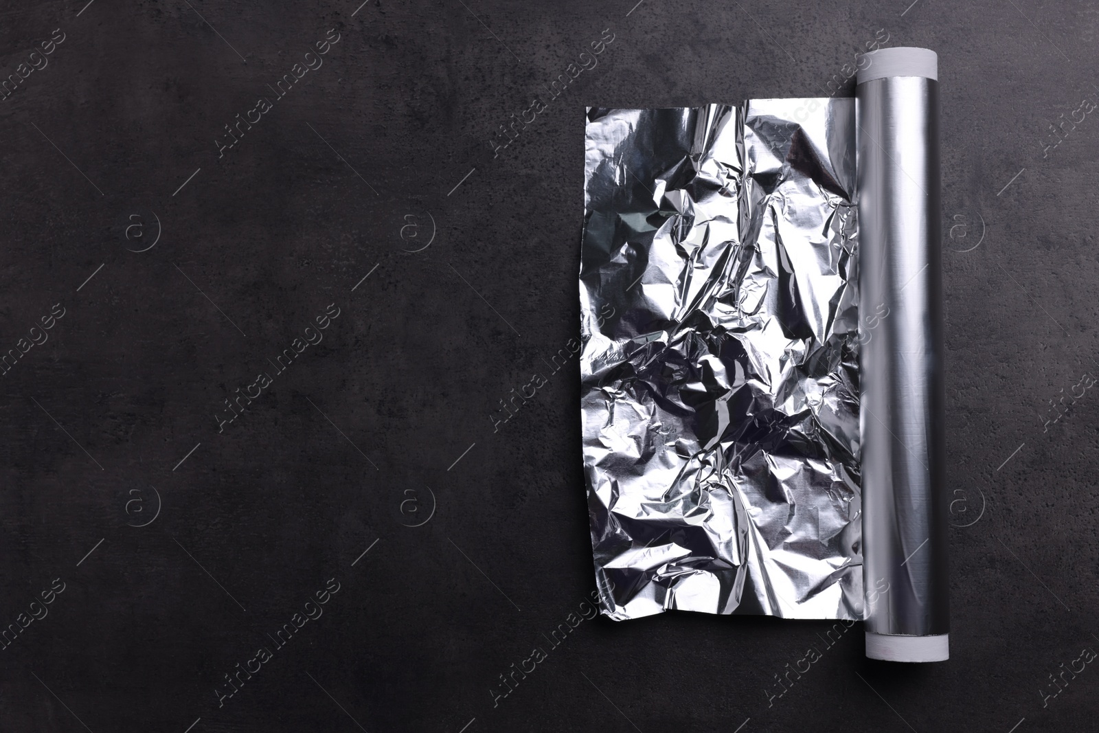 Photo of Roll of aluminum foil on dark grey table, top view. Space for text