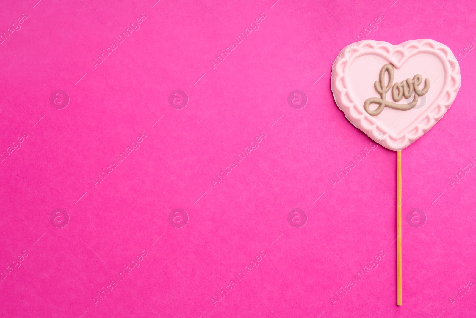 Photo of Chocolate heart shaped lollipop with word Love on pink background, top view. Space for text
