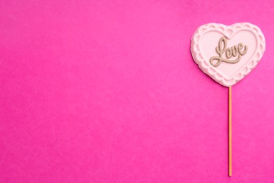 Chocolate heart shaped lollipop with word Love on pink background, top view. Space for text