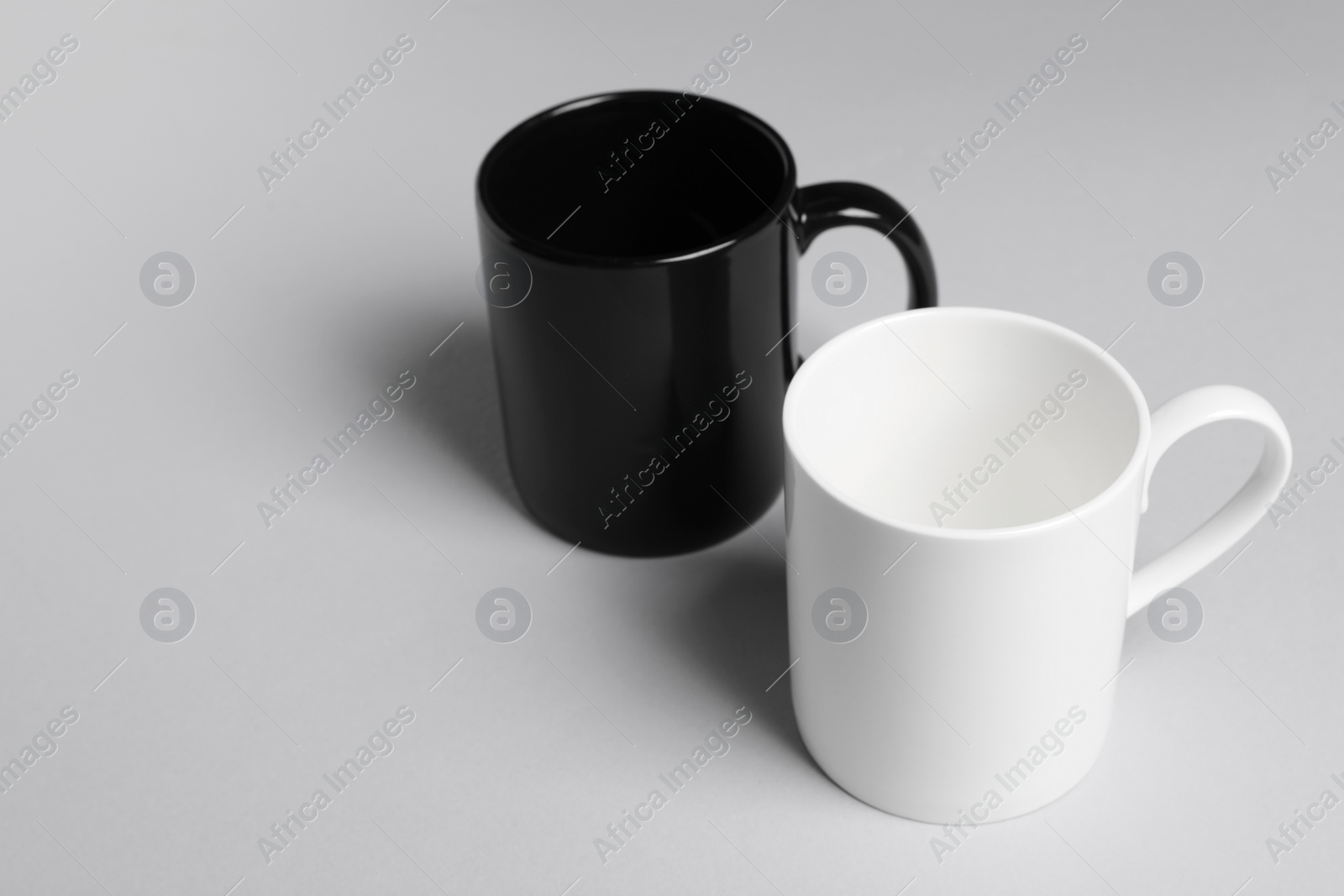 Black and white ceramic mugs on light background. Space for text Photo of Black and white ceramic mugs on light background. Space for text
