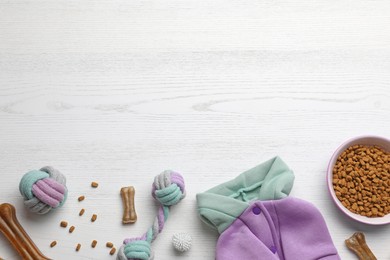 Photo of Flat lay composition with dog clothes, food and accessories on white wooden table. Space for text