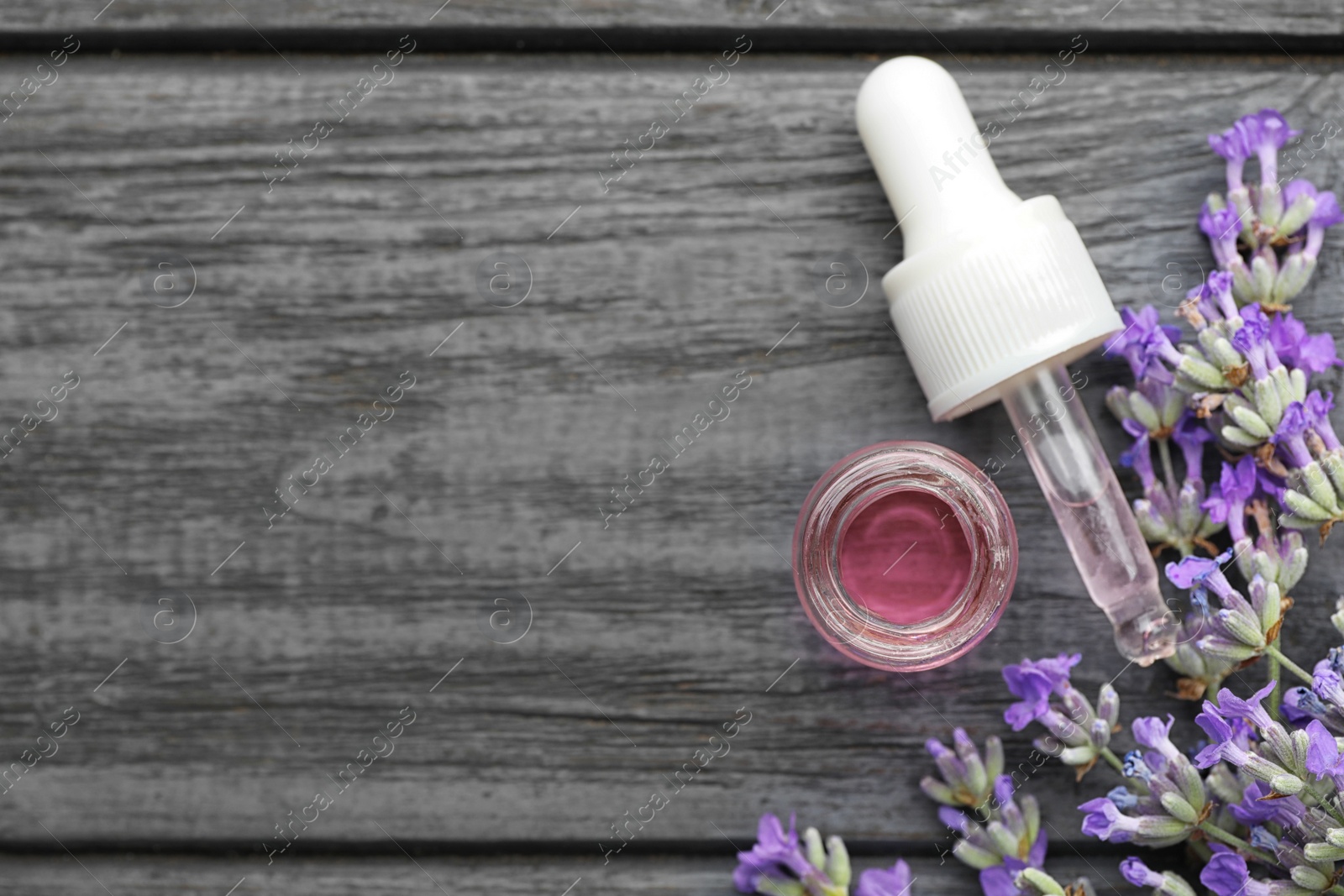 Photo of Bottle with natural lavender oil, dropper and flowers on grey wooden table, flat lay. Space for text