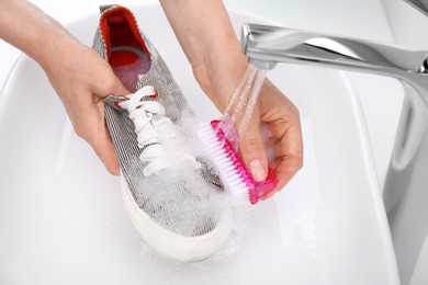 Photo of Woman washing shoe with brush under tap water in sink, closeup