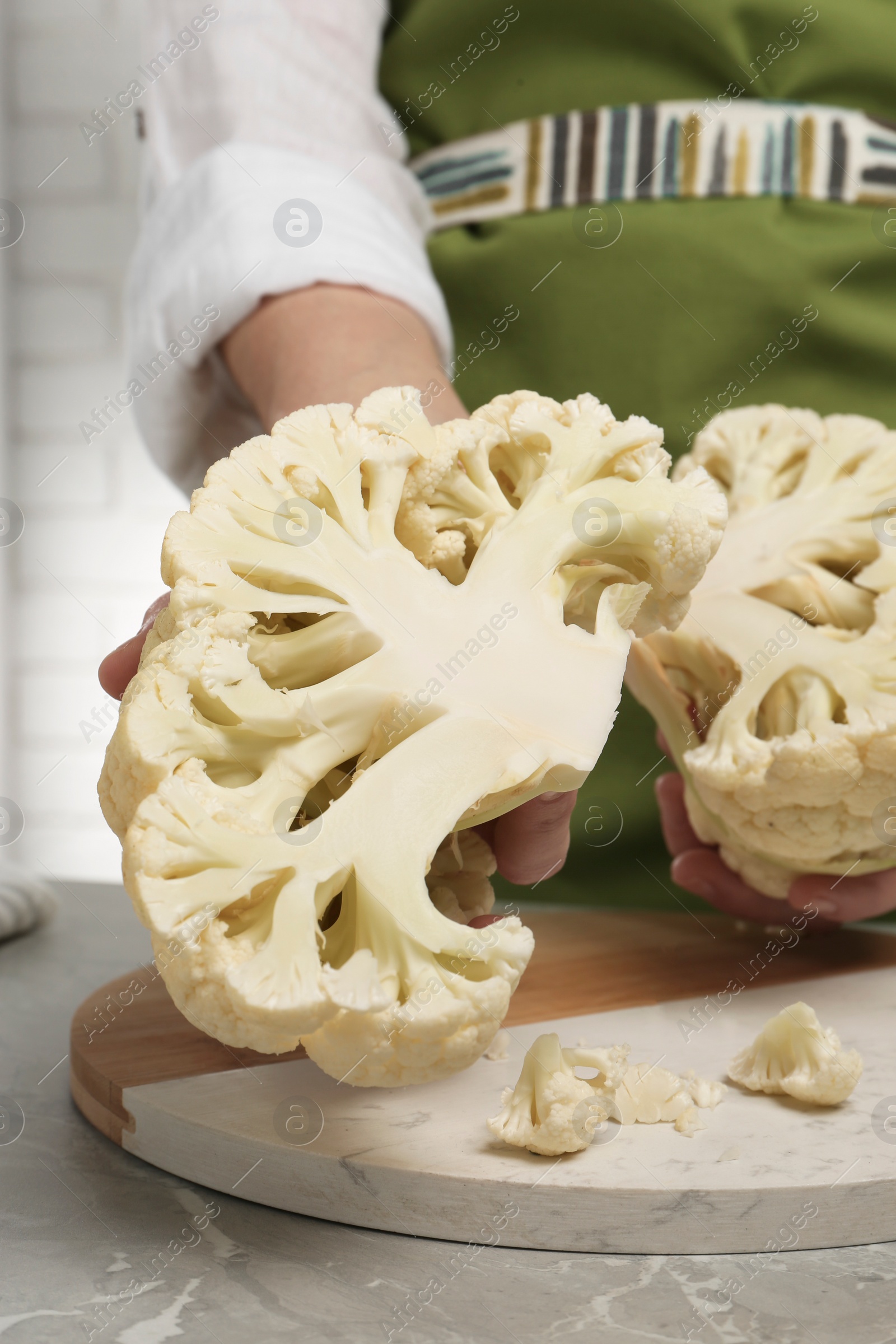 Photo of Woman holding halves of fresh cauliflower at light grey table, closeup