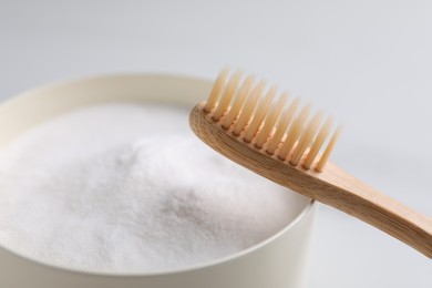 Photo of Bamboo toothbrush and bowl of baking soda on white background, closeup